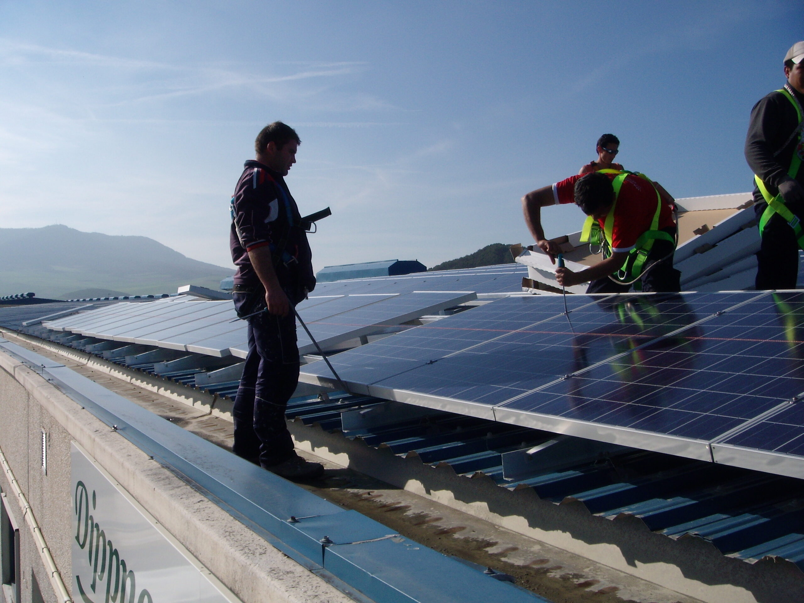 Workers installing solar panels on a rooftop with mountains in the background.
